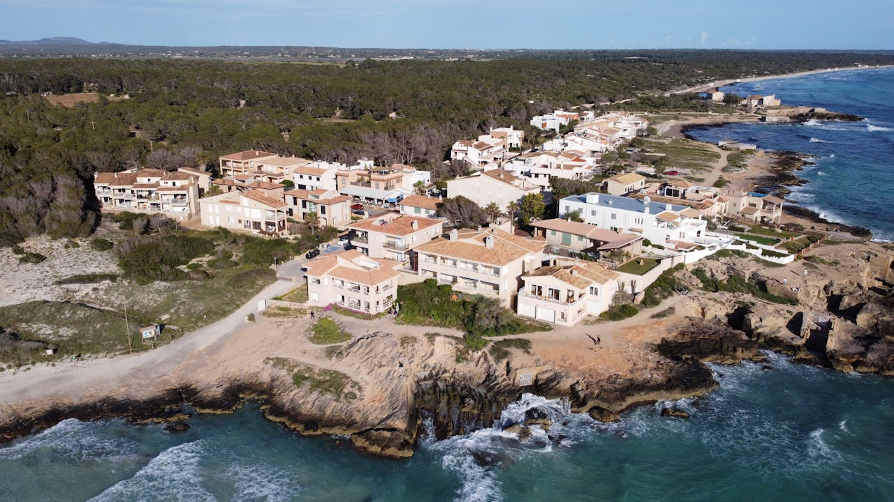 services-01 Scenic aerial view of a coastal village in Ses Covetes, Spain, showcasing the Mediterranean shoreline and architecture.